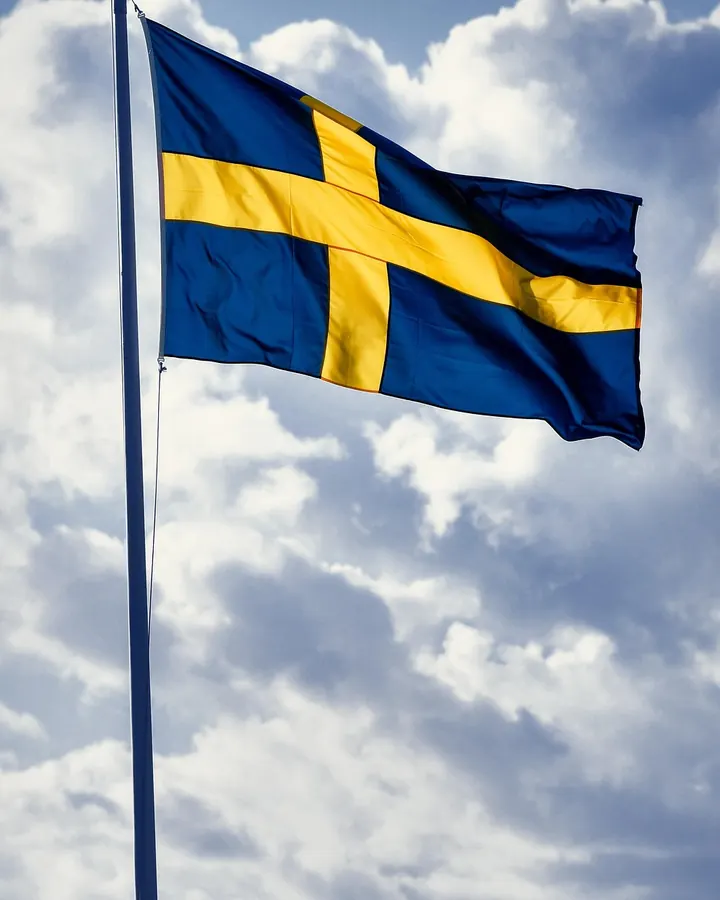 Svenska flaggan på flaggstång mot ett molnigt blått himmel