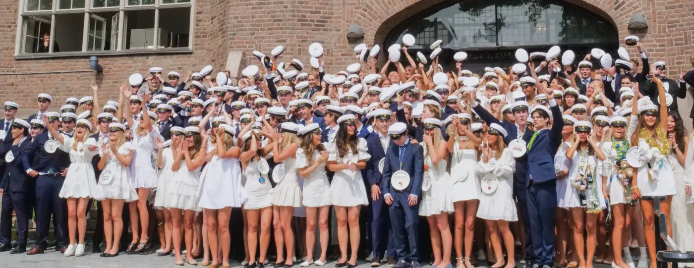 Avgångselever i vita studentmössor framför en tegelbyggnad